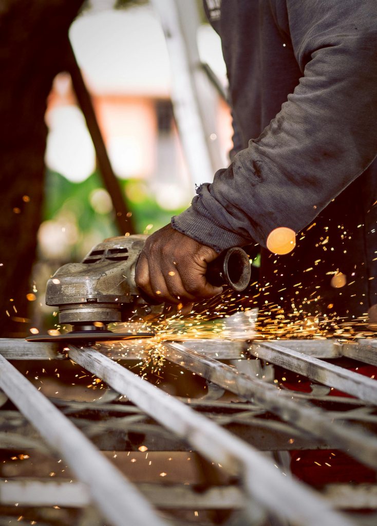 Close-up of a worker using a grinder on metal with sparks flying in a workshop setting.